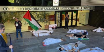 Bandiere palestinesi e corpi a terra avvolti da teli bianchi